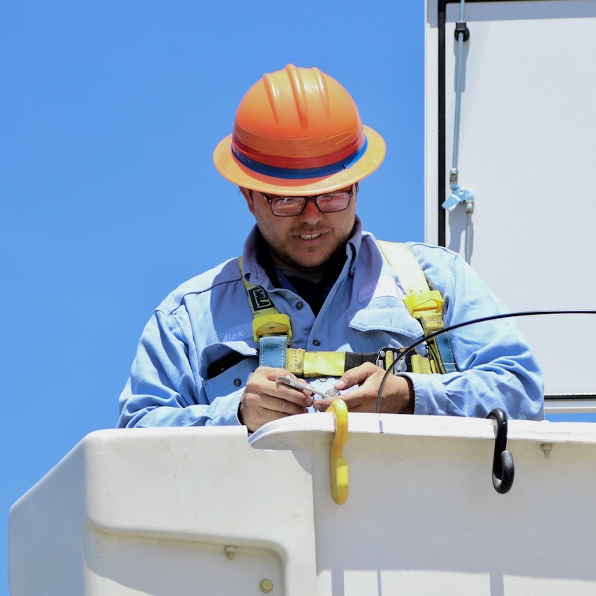 Man wearing orange hardhat in bucket truck working on fiber network.